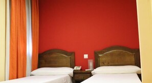 Une chambre d’hôtel avec deux lits, une tête de lit en bois, une table de chevet avec un téléphone et un mur rouge.