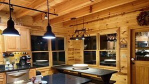A wooden cabin-style kitchen with a central island, pendant lighting, and large windows. - LARGE elegant DESIGNER mountain cabin home on RIVER COOSAWATTEE perfect4families (ellijay)