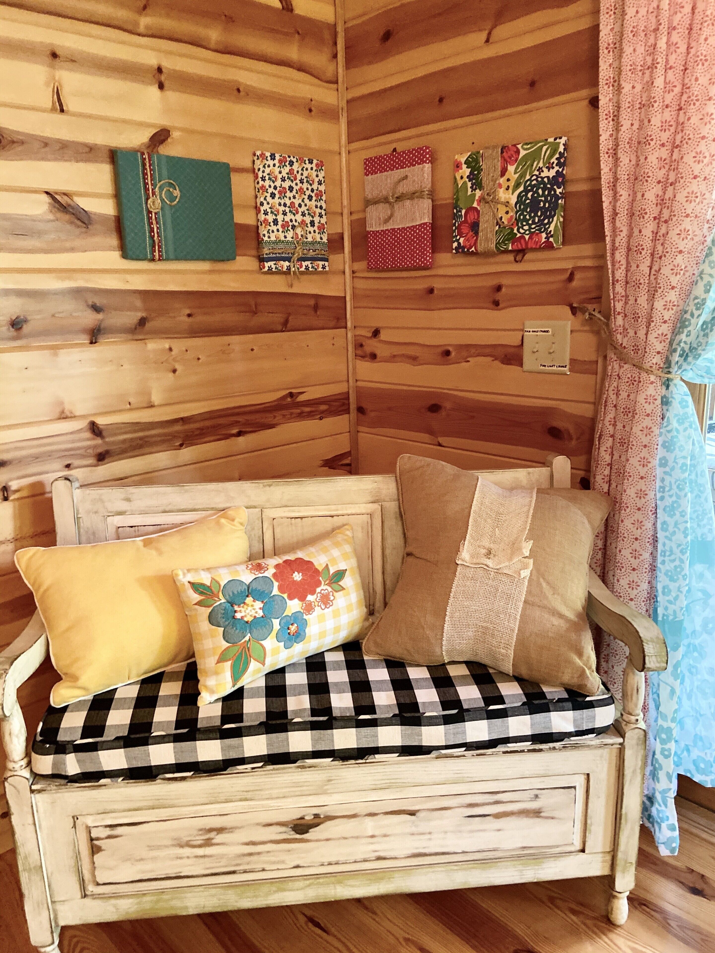 A rustic wooden room with a vintage-style sofa, decorative pillows, and wall-mounted art pieces.