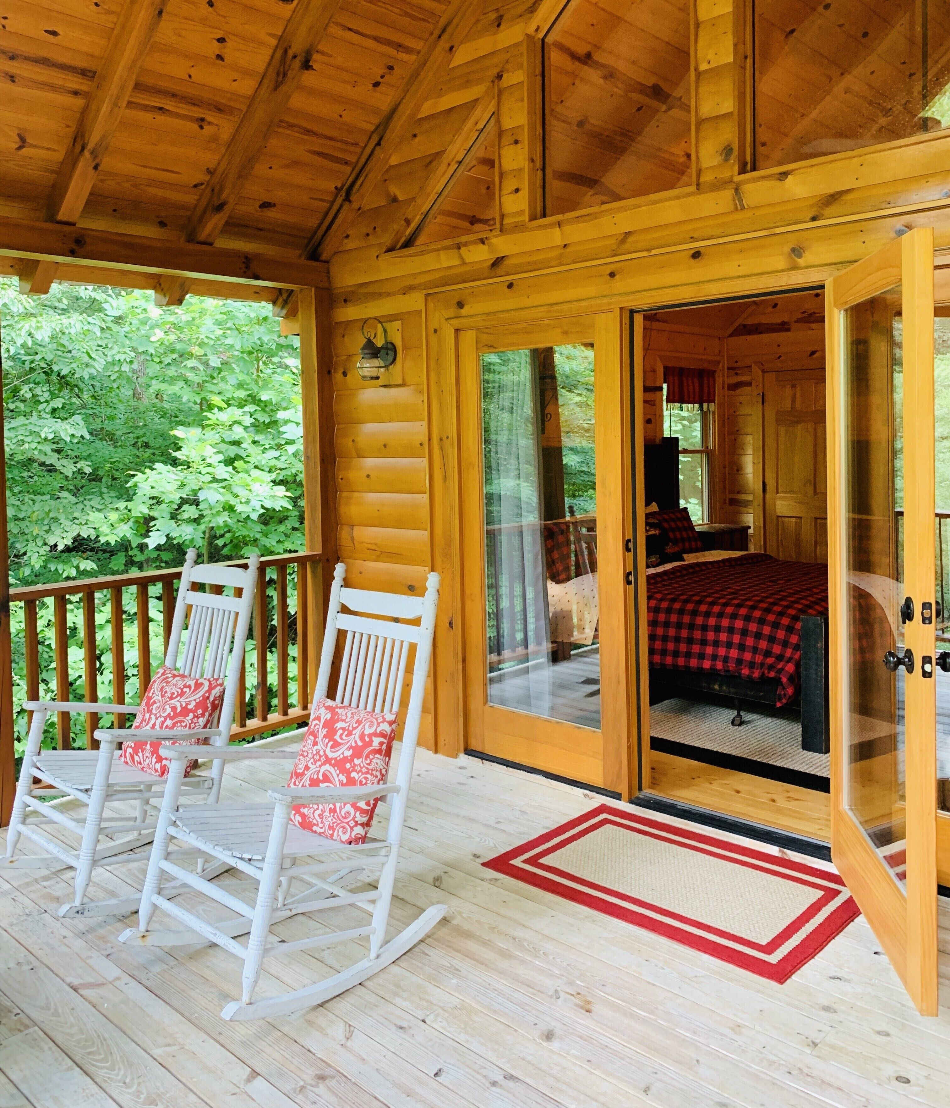 Une cabane en bois dotée d’un porche avec des fauteuils à bascule et d’un lit recouvert d’une couverture à carreaux.