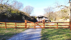 Un chemin de gravier mène à une porte en bois, avec une grange en arrière-plan.