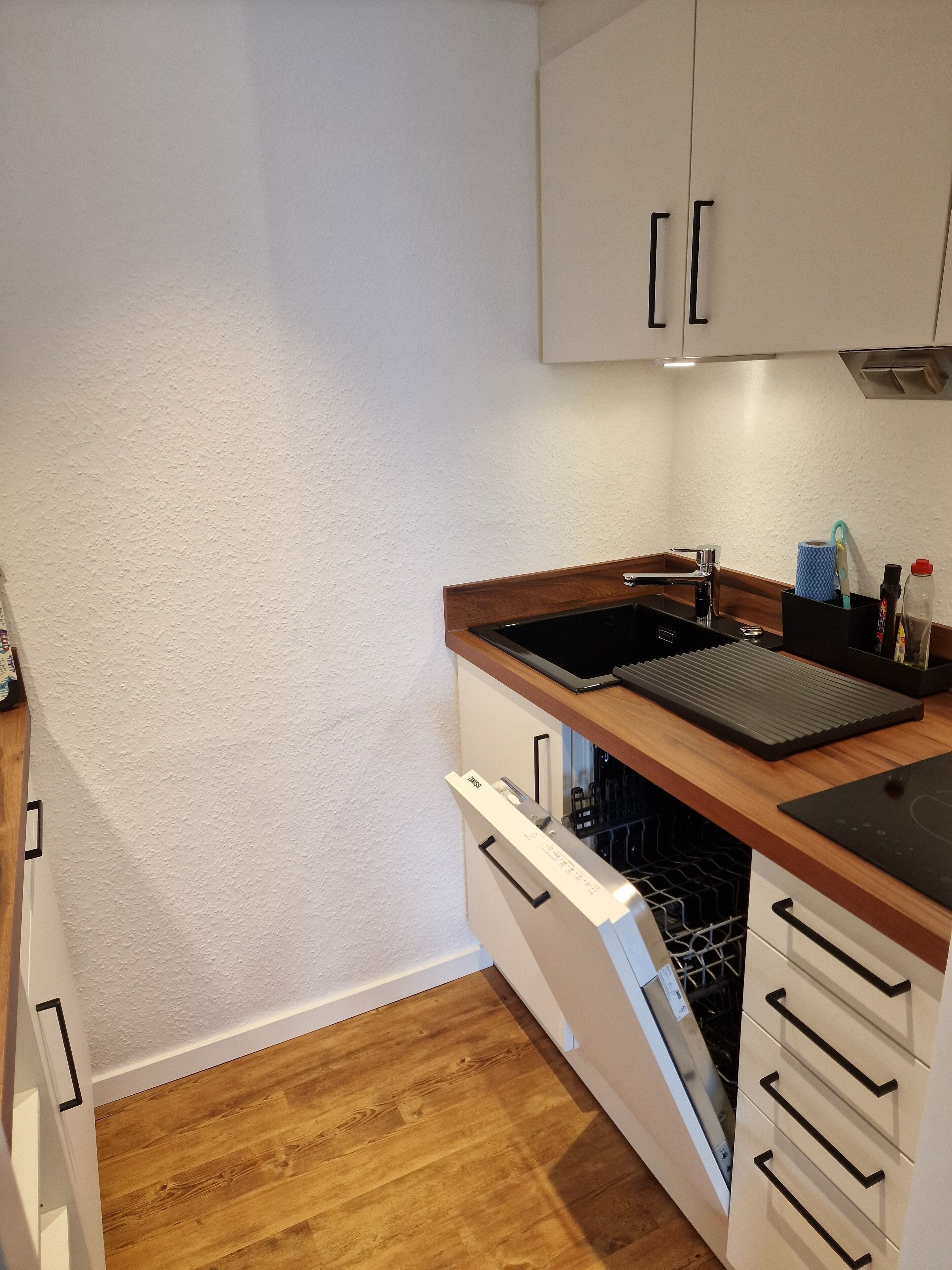 A compact kitchen with white cabinets, a wooden countertop, a built-in dishwasher, and a sink.