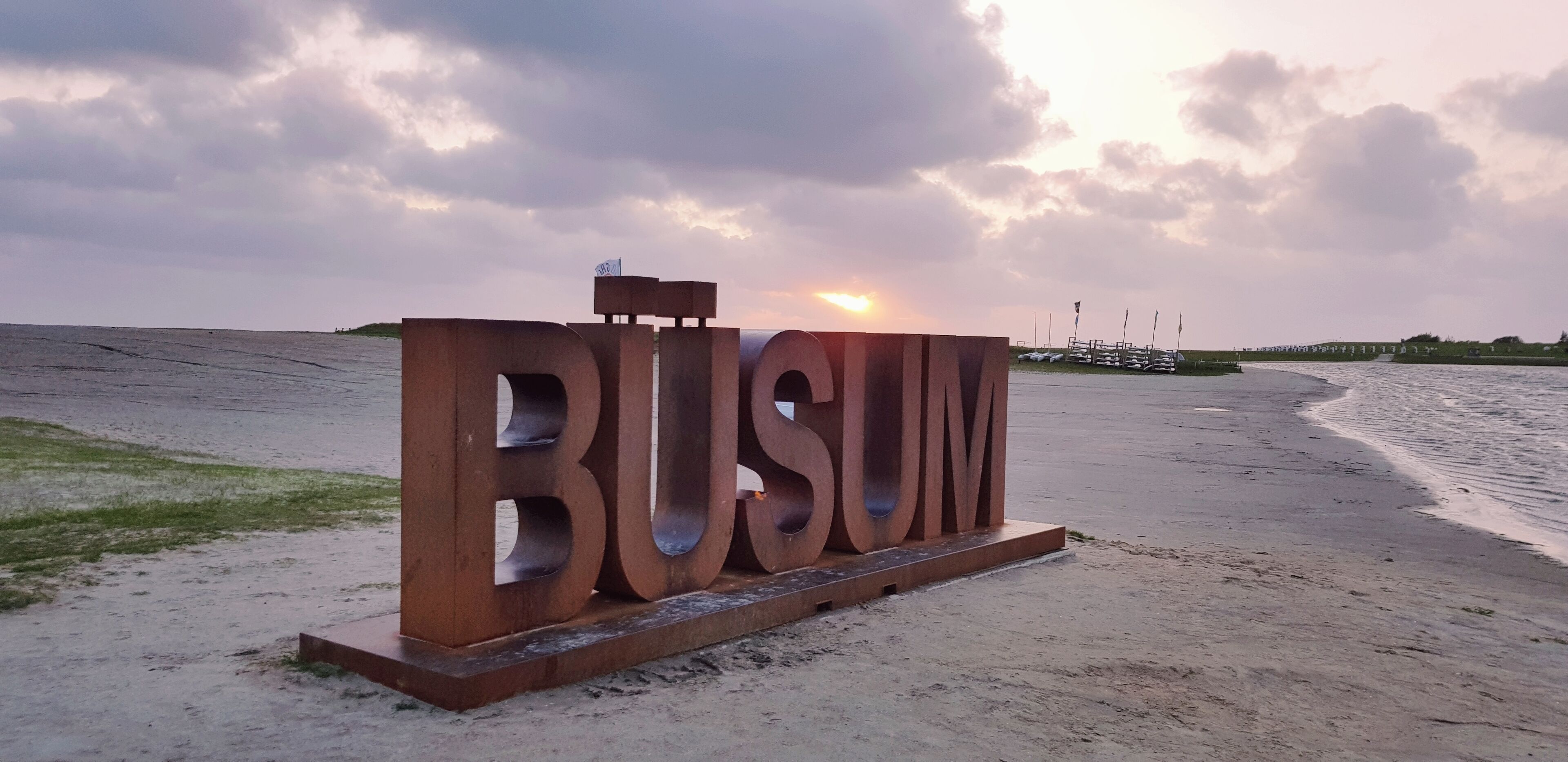 Ein großes Metallschild mit dem Wort "BUSUM" am Strand.