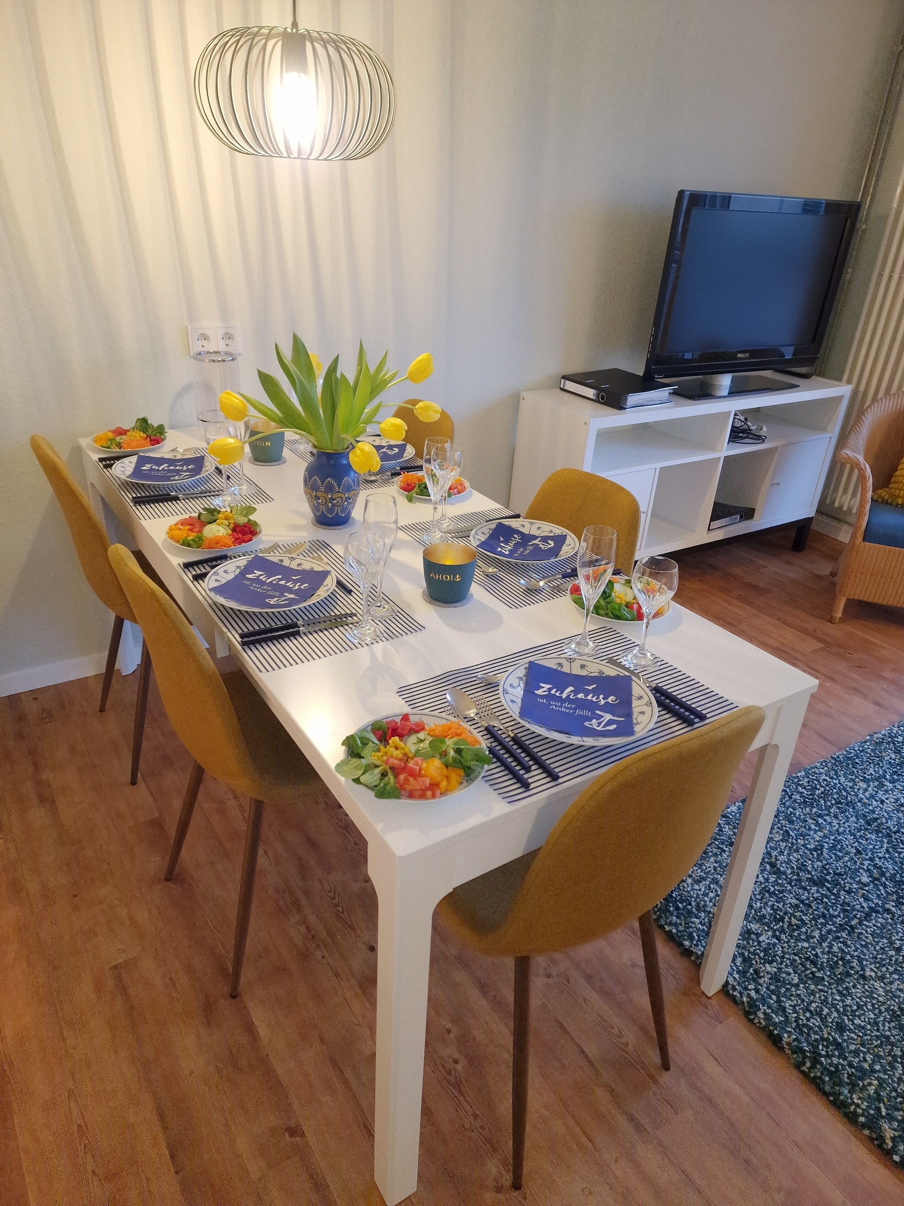 Une table à manger dressée avec des assiettes, des couverts et un vase rempli de fleurs jaunes.
