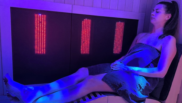 A person seated in a room with a large, illuminated panel and a bench.