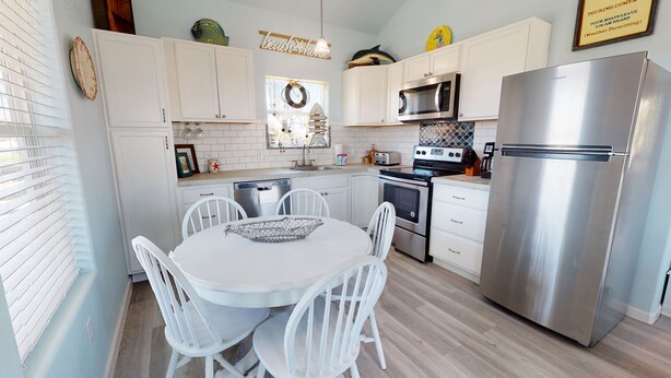 Een moderne keuken met witte kasten, roestvrijstalen apparatuur en een ronde eettafel met stoelen.