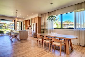 Uma cozinha moderna com armários de madeira, uma ilha grande e uma área de jantar com mesa e cadeiras de vidro.