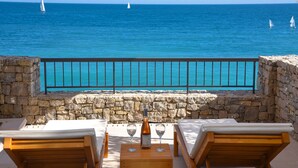 A stone balustrade overlooking a sea with sailboats, a wooden table with two glasses and a bottle, and two lounge chairs. - Lustica Bay Marina (Radovici)