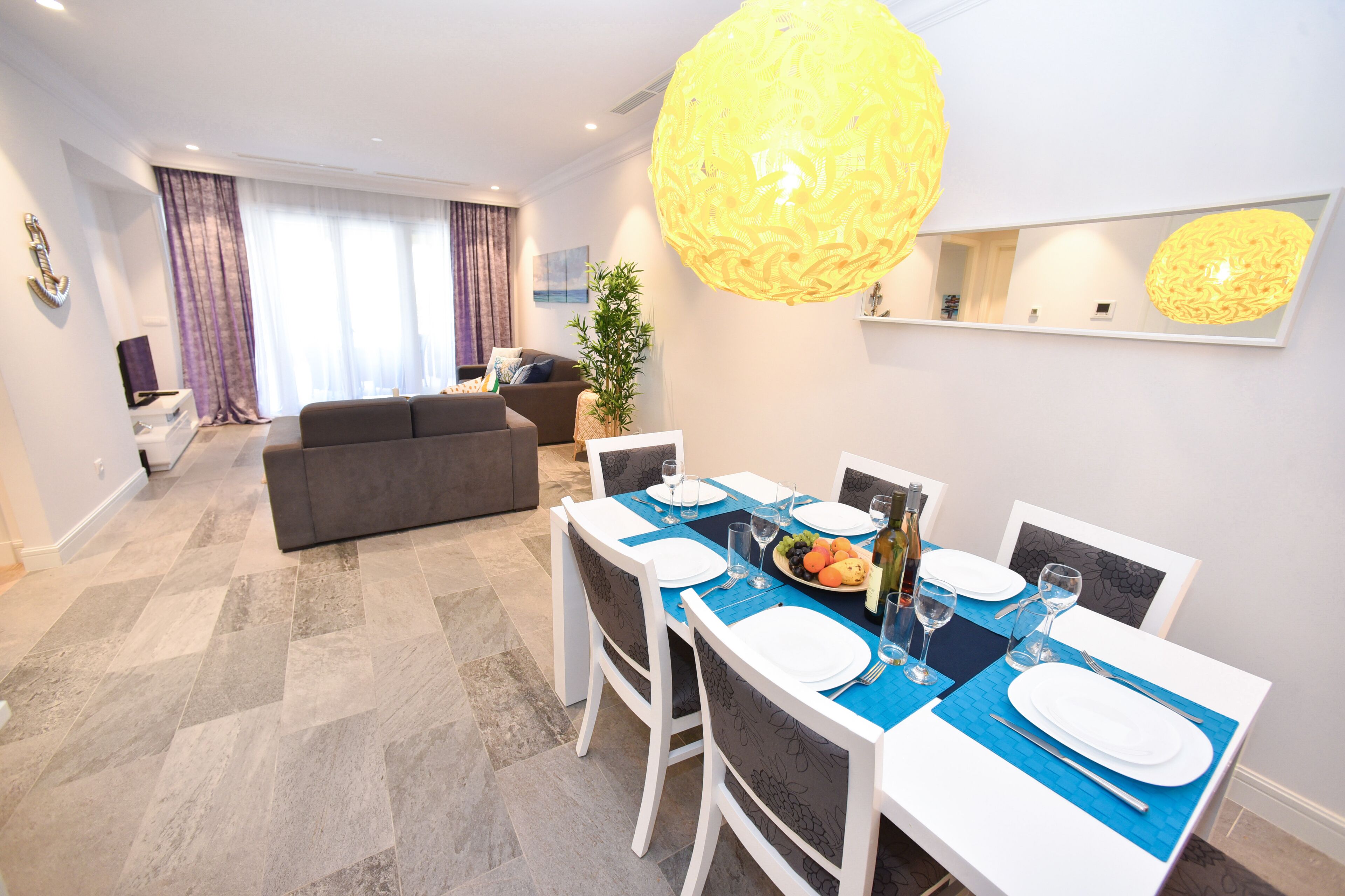 A modern dining area with a table set for four, a sofa, and a large decorative light fixture.