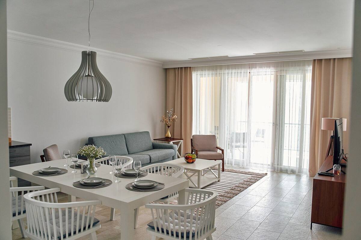 A modern living room with a dining area, featuring a sofa, a coffee table, and a dining table set for four.