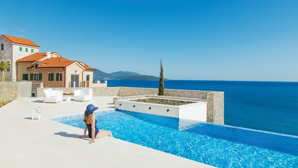 A poolside area with a view of the sea, a building with a red roof, and a woman in a blue swimsuit. - Lustica Bay Marina (Radovici)