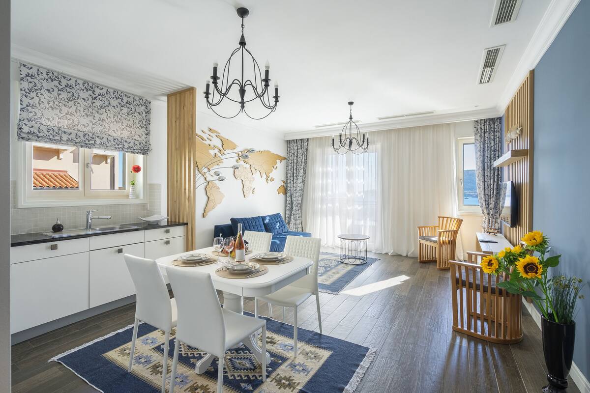 A modern kitchen with white cabinets, a dining area with a white table and chairs, and a living area with a blue sofa and a world map on the wall.