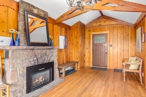 A log cabin interior with a stone fireplace, wooden walls, a bench, and a door with a window.