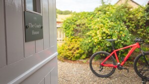 Ein Schild mit der Aufschrift "The Coach House" an einem Gebäude, ein rotes Fahrrad und ein Garten mit üppiger Bepflanzung.