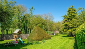 A well-maintained garden with a wooden play structure, a neatly trimmed hedge, and a stone wall.