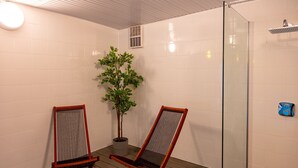 Ett badrum med två trästolar, en krukväxt och en duschavdelning med glasväggar.