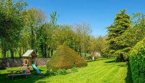 Un jardin bien entretenu, agrémenté d’une structure de jeu en bois, d’un arbuste taillé avec soin et d’un mur en pierre.
