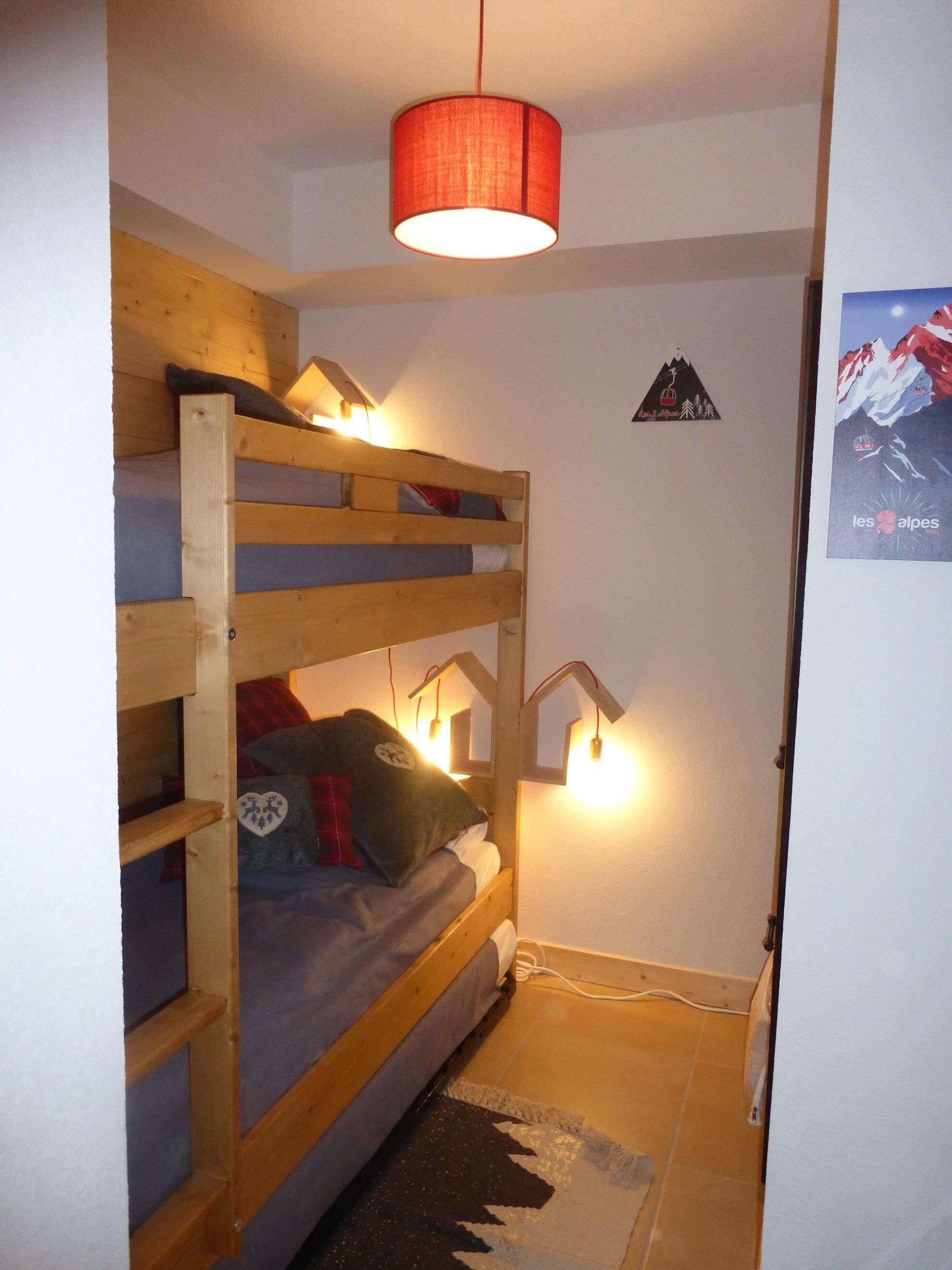 Una stanza piccola con un letto a castello, una lampada a sospensione, un poster sul muro e una presa di corrente a pavimento.