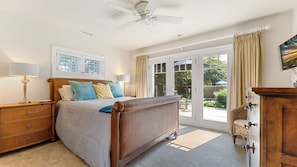 Quarto com cama, mesas de cabeceira, penteadeira, ventoinha no teto e vista para o exterior.