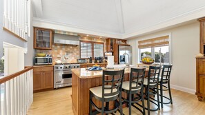 A spacious kitchen with wooden cabinets, a large island with bar stools, and a view of the outdoors. - Magnificient Luxurious Home with Built-in Pool on the Beach (Villas)