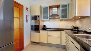 A compact kitchen with stainless steel appliances, wooden cabinets, and a tiled floor.