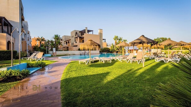 Een zwembadgedeelte van een resort, met ligbedden, een zwembad en een gebouw met een stenen gevel.