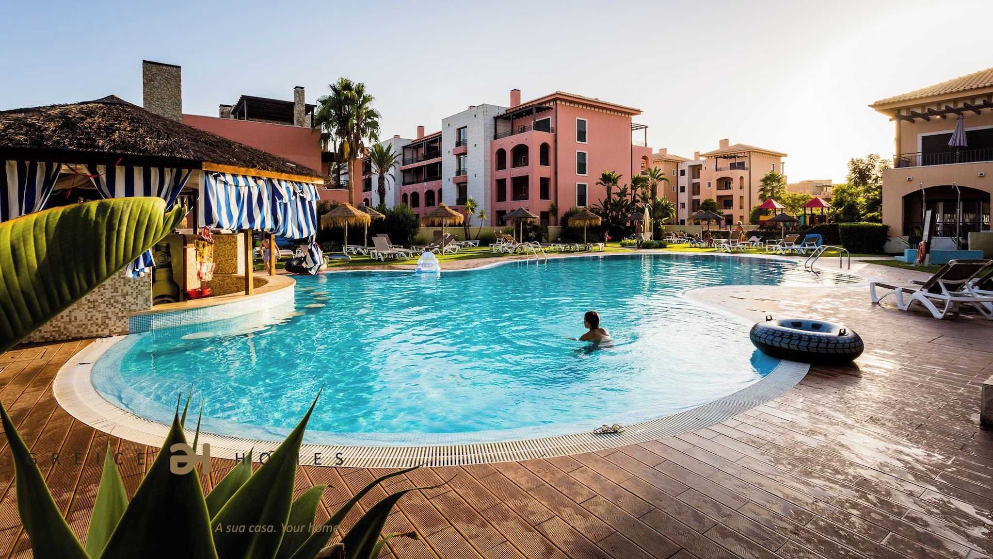A swimming pool with lounge chairs and umbrellas, surrounded by buildings with balconies.