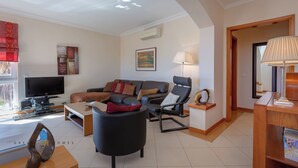 Een moderne woonkamer met een flatscreen televisie, een zithoek, een zwarte fauteuil en een salontafel.