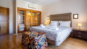 Een slaapkamer met een bed, nachtlampjes, een houten garderobe en een geboeide plaid op de vloer.
