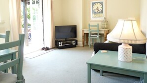 A living room with a television, a table with a lamp, a chair, and a suitcase.