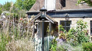 A traditional house with a front porch, a small garden with various plants, and a visible chimney.