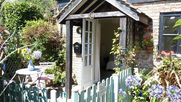 A quaint cottage with a small porch, a mailbox, and a garden with various plants and flowers.