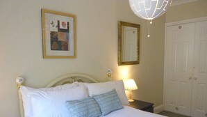 A neatly made bed with white and blue bedding, a bedside lamp, a framed picture on the wall, and a door in the background.
