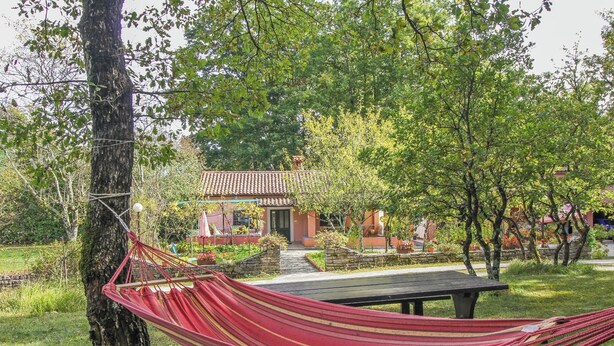 Un hamac est attaché à un arbre dans un jardin, avec un bâtiment visible en arrière-plan.