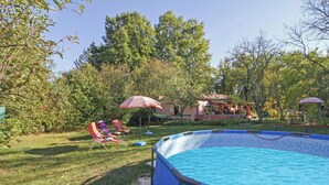 Un jardin avec une piscine, des chaises longues et des parasols.