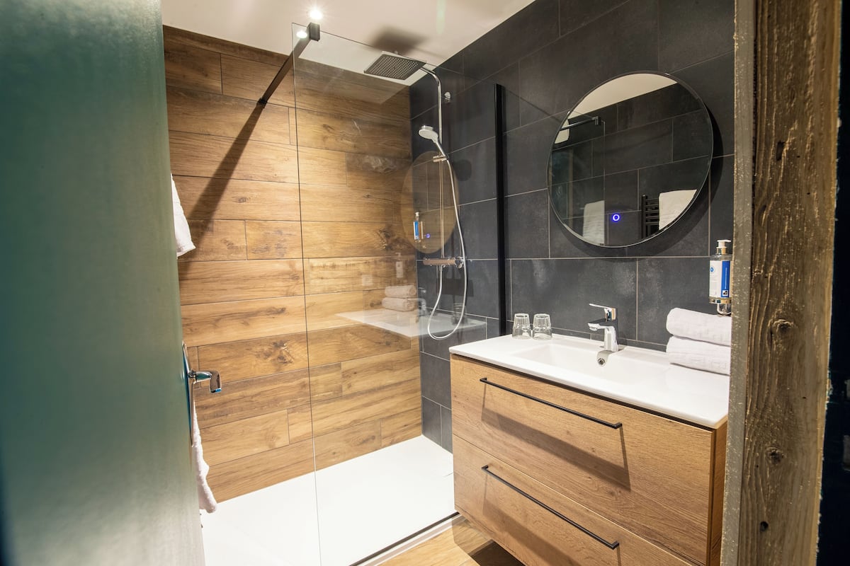 Un baño moderno con tocador de madera, un espejo redondo y una ducha.