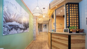 Un espace d’accueil avec un comptoir en bois, un grand tableau représentant un paysage de montagne et des lampes en osier suspendues.