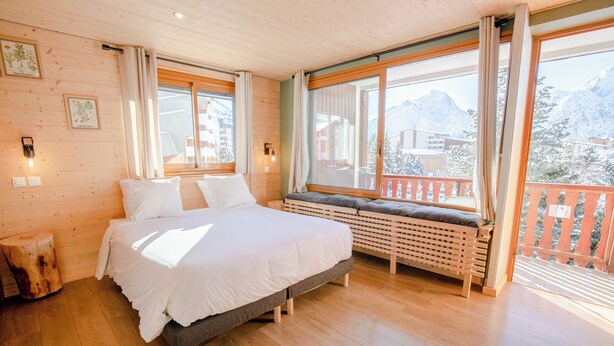 Une chambre avec un grand lit, un plancher en bois et une fenêtre donnant sur les montagnes.