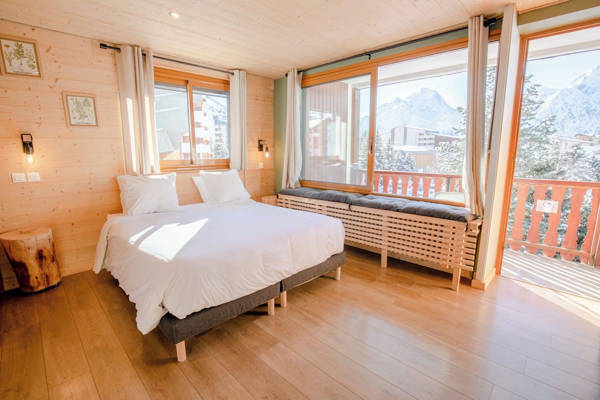 Un dormitorio con una cama grande, suelo de madera y ventana con vistas a montañas.
