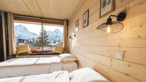 Une chambre avec deux lits, des murs en bois, une fenêtre donnant sur la montagne et un luminaire fixé au mur.