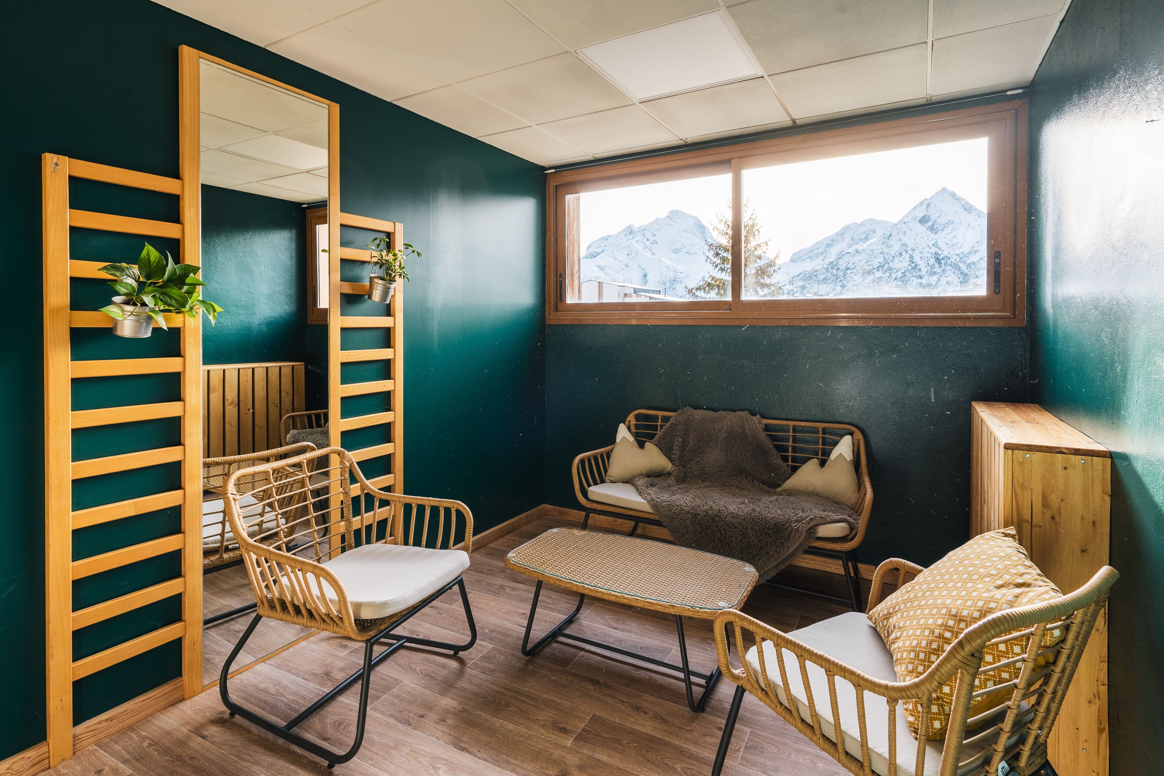 Une pièce chaleureuse avec un grand miroir, des meubles en osier, une petite table et une fenêtre donnant sur les montagnes.