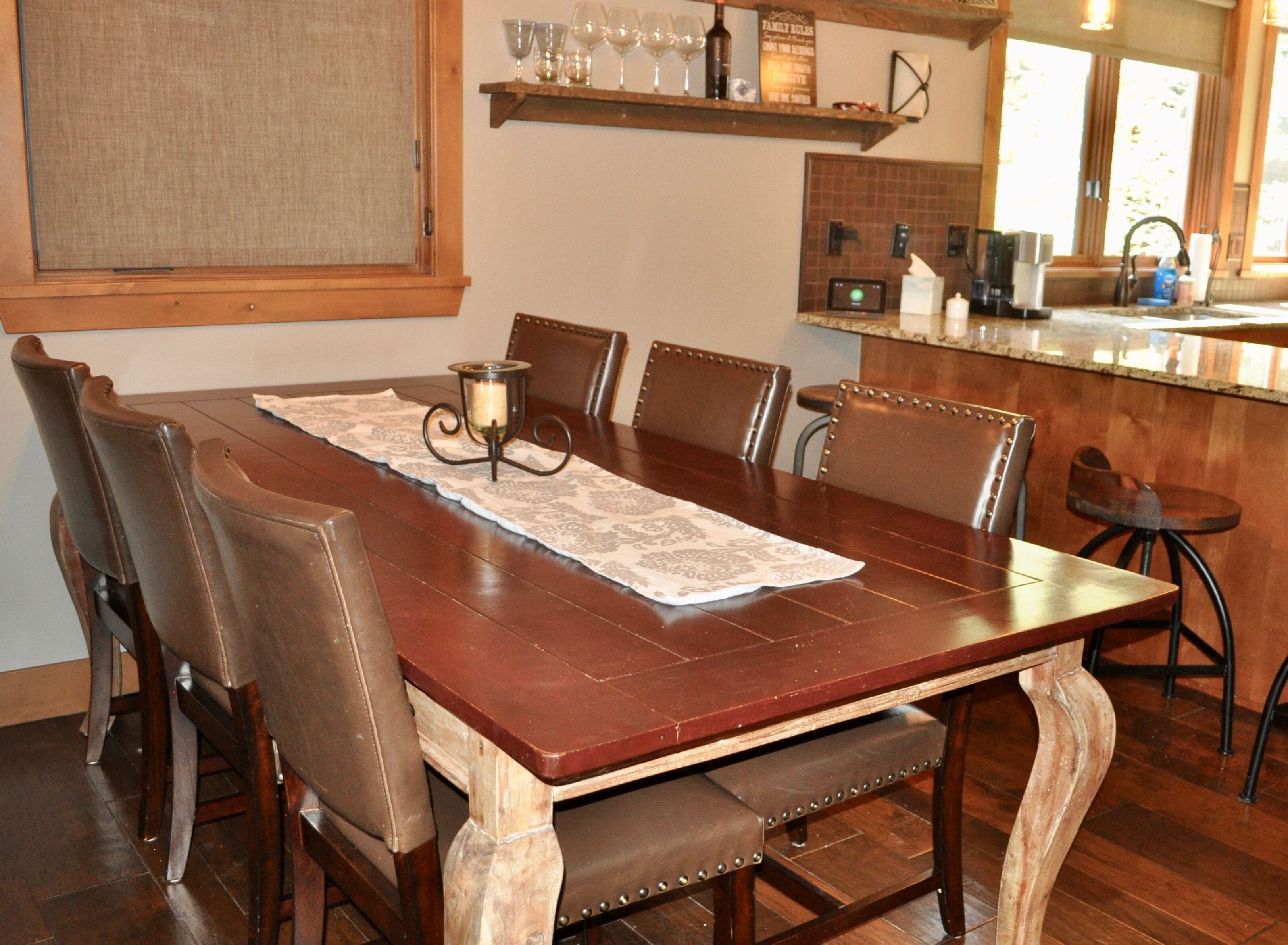 A dining area with a wooden table, six chairs, a candle holder, and a kitchen in the background.