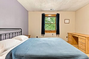Un dormitorio con cama, una ventana con cortinas, un aparador de madera y un cuadro colgado en la pared.