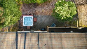 A rooftop with a hot tub, a wooden deck, and surrounding trees. - River Cabin w/hot tub, fire pit, deck, games, wifi (Great Cacapon)