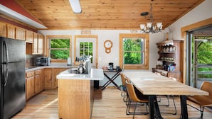 Een keuken met houten kastjes, een centraal eiland, een eettafel met stoelen, een koelkast en een klok aan de muur.