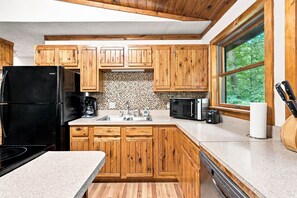 Una cocina con armarios de madera, un refrigerador, una cafetera, un microondas y un ventanal con vista a follaje.