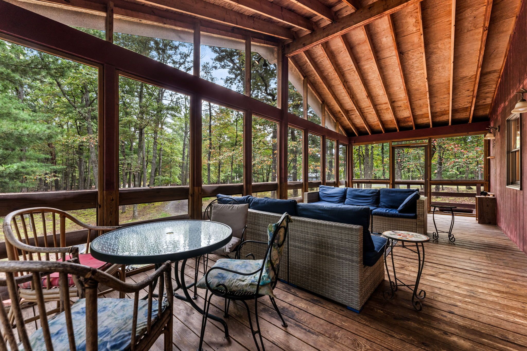 Un espacio de estar techado al aire libre con piso de madera, muebles de mimbre y una mesa de vidrio.