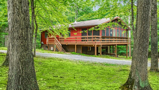 A cabin with a wooden deck, a staircase, and a view of the surrounding forest. - River Cabin w/hot tub, fire pit, deck, games, wifi (Great Cacapon)