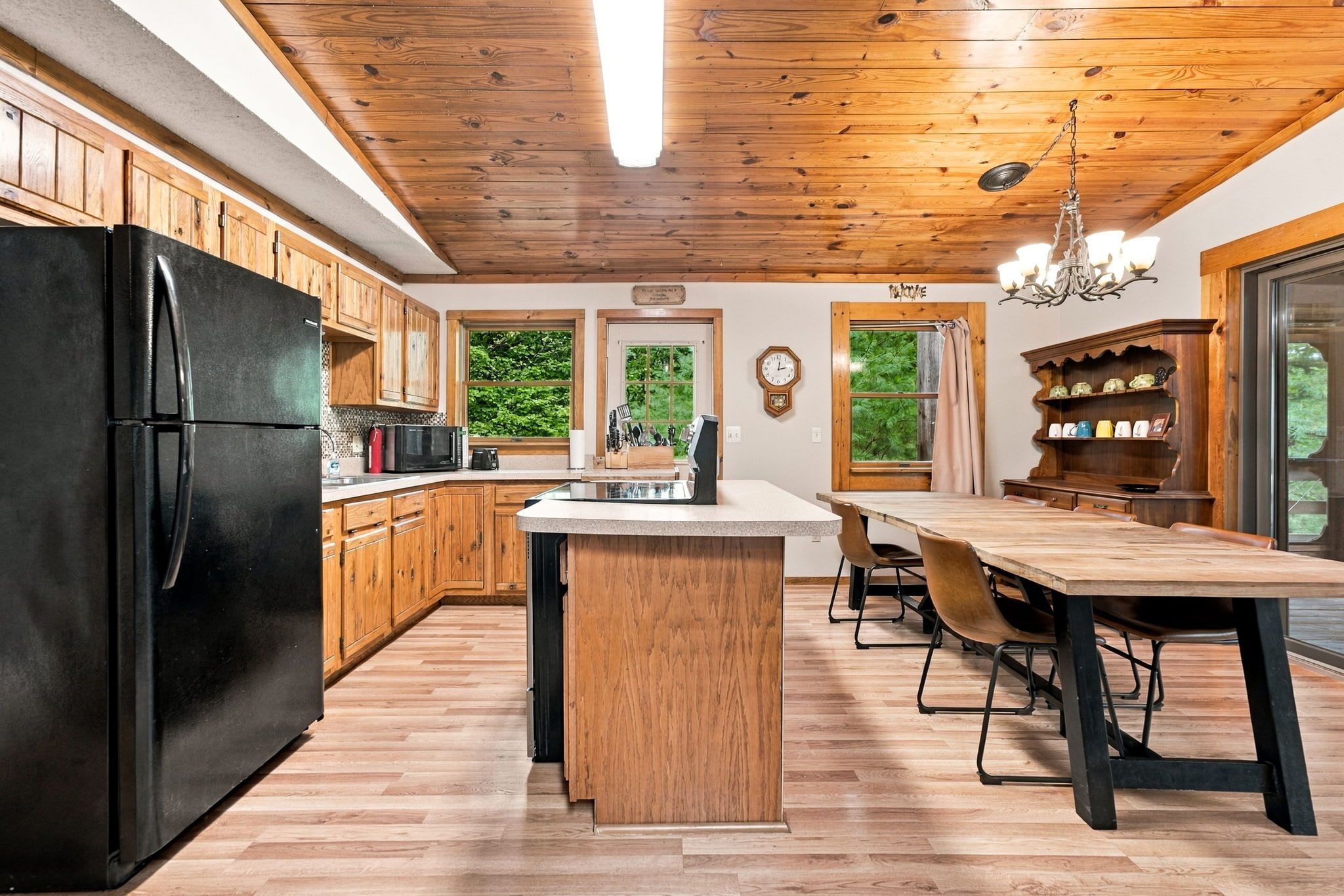 Eine Küche mit Holzausstattung, einem schwarzen Kühlschrank, einer Mikrowelle und einem Essbereich mit Holztisch und Stühlen.
