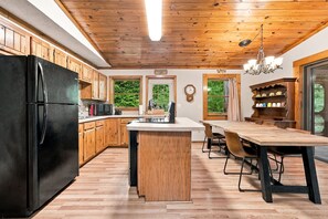 Una cocina con armarios de madera, un refrigerador negro, un microondas y un comedor con una mesa y sillas de madera.